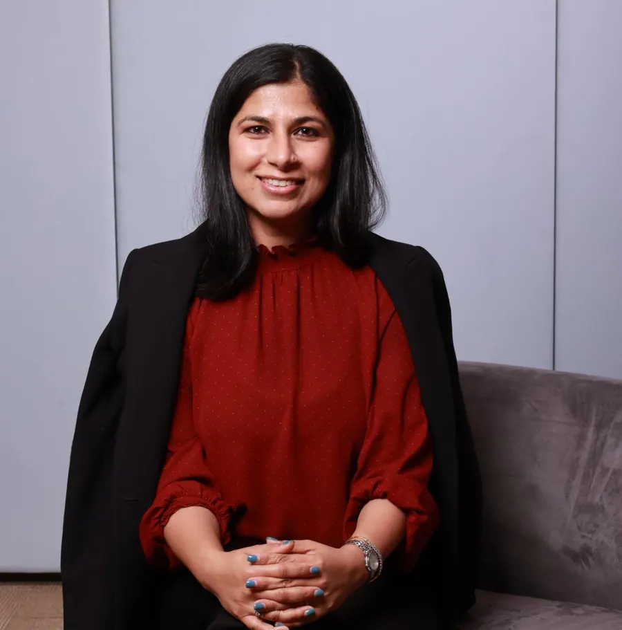 Priya Mann, smiling, seated on a sofa