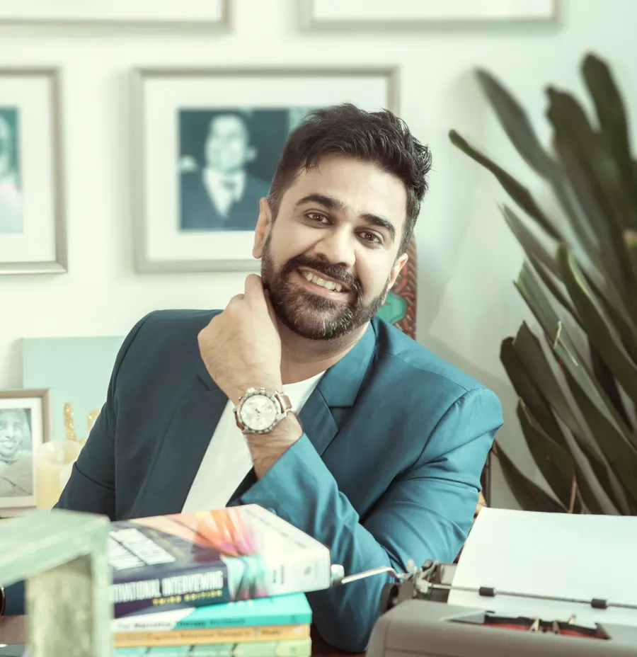 Rohan Mann at his desk in a teal blazer, smiling