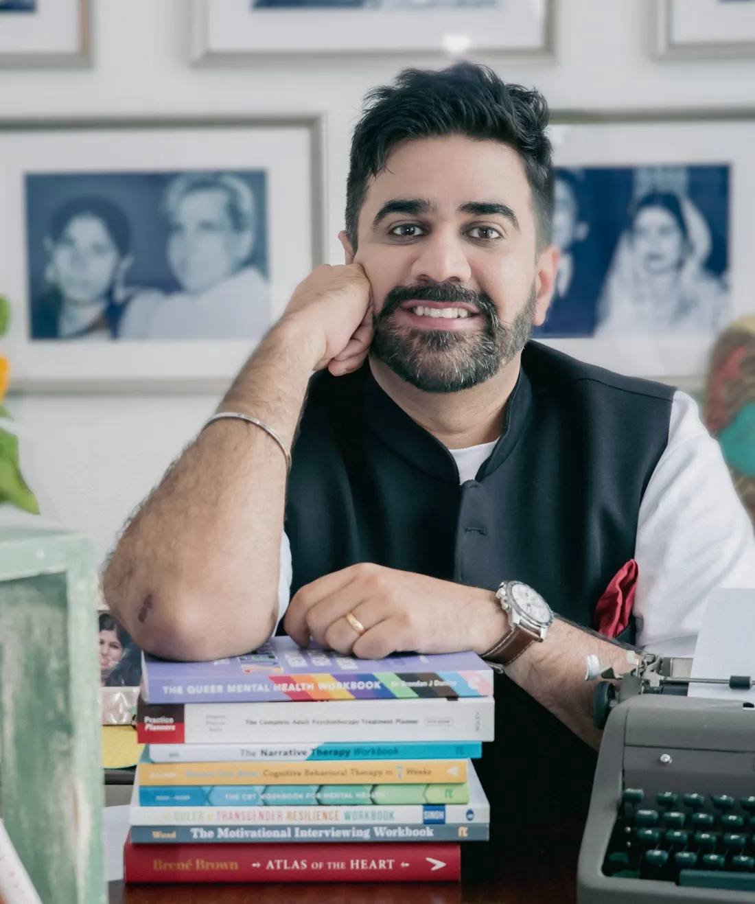 Rohan Mann at his desk, smiling, with a stack of therapy books and a typewriter